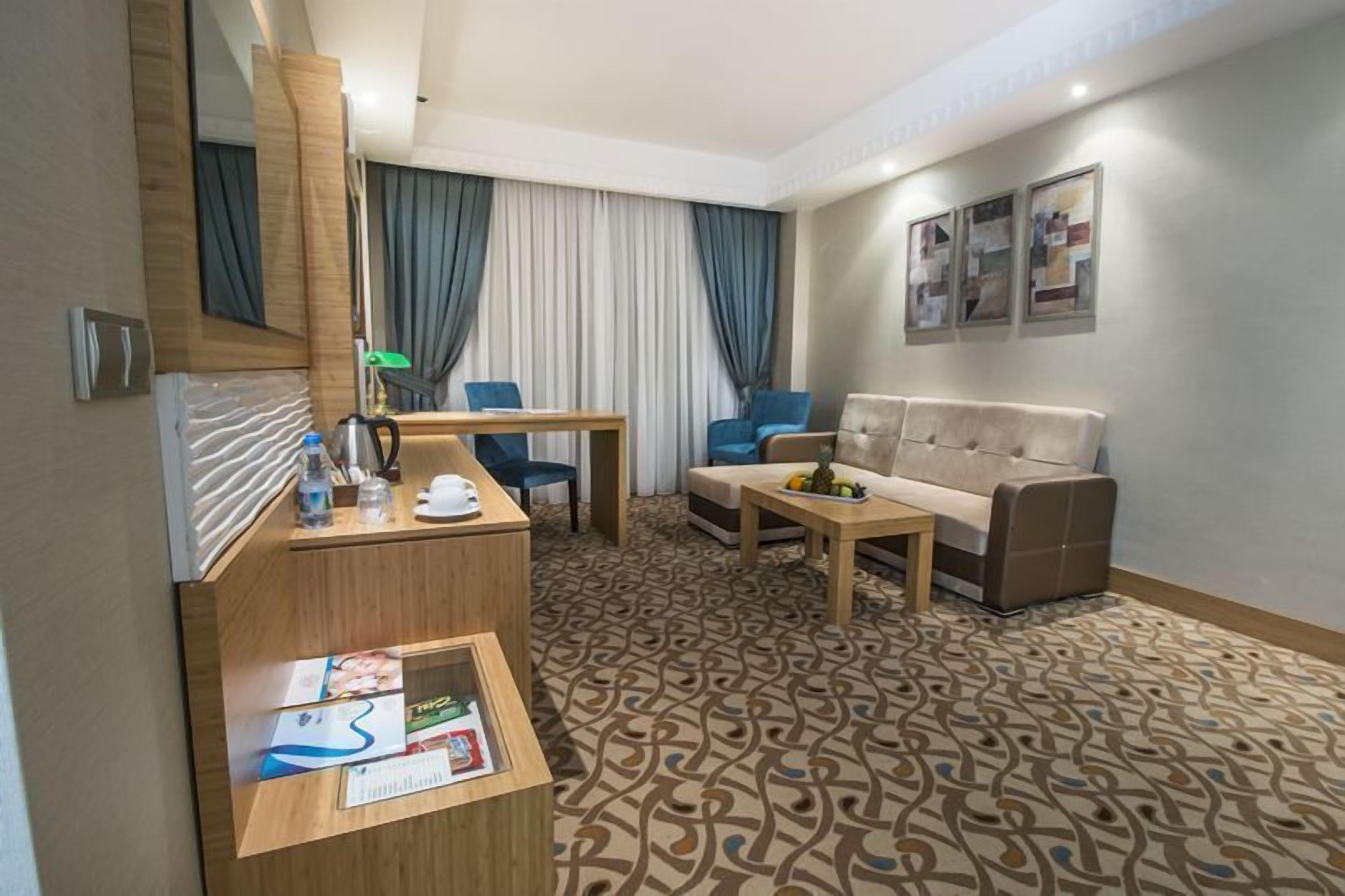 A hotel room with a wooden desk, a sofa, a coffee table, and a patterned carpet.