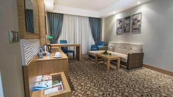 A hotel room with a wooden desk, a sofa, a coffee table, and a patterned carpet.