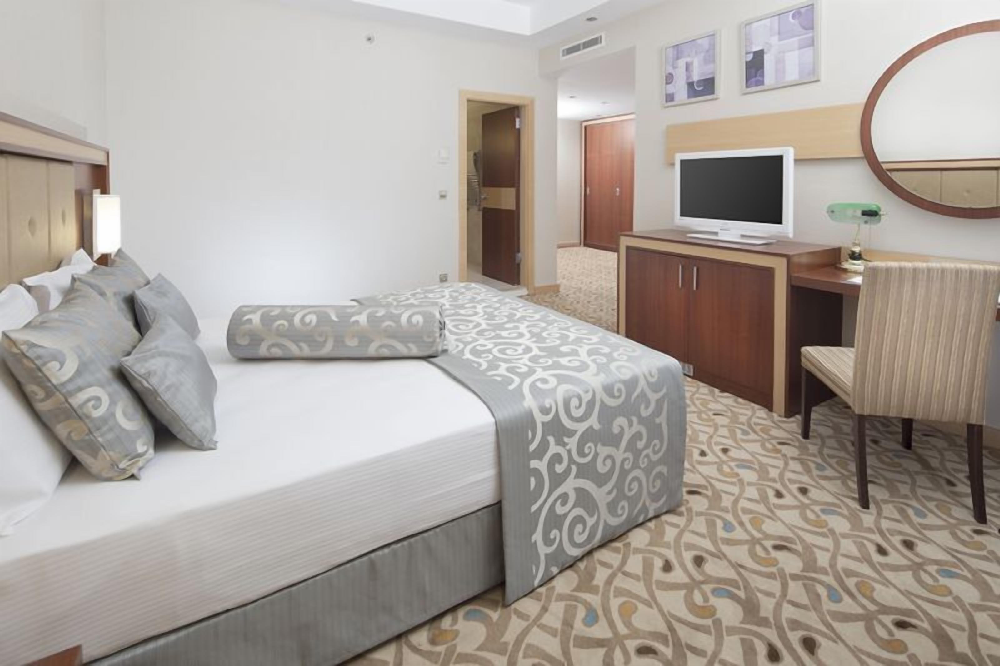 Una habitación de hotel con una cama, un escritorio con una computadora, un televisor y una silla.