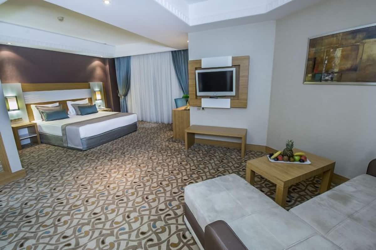 Ein Hotelzimmer mit Bett, Fernseher, kleinem Tisch mit Früchten und einer Couch.