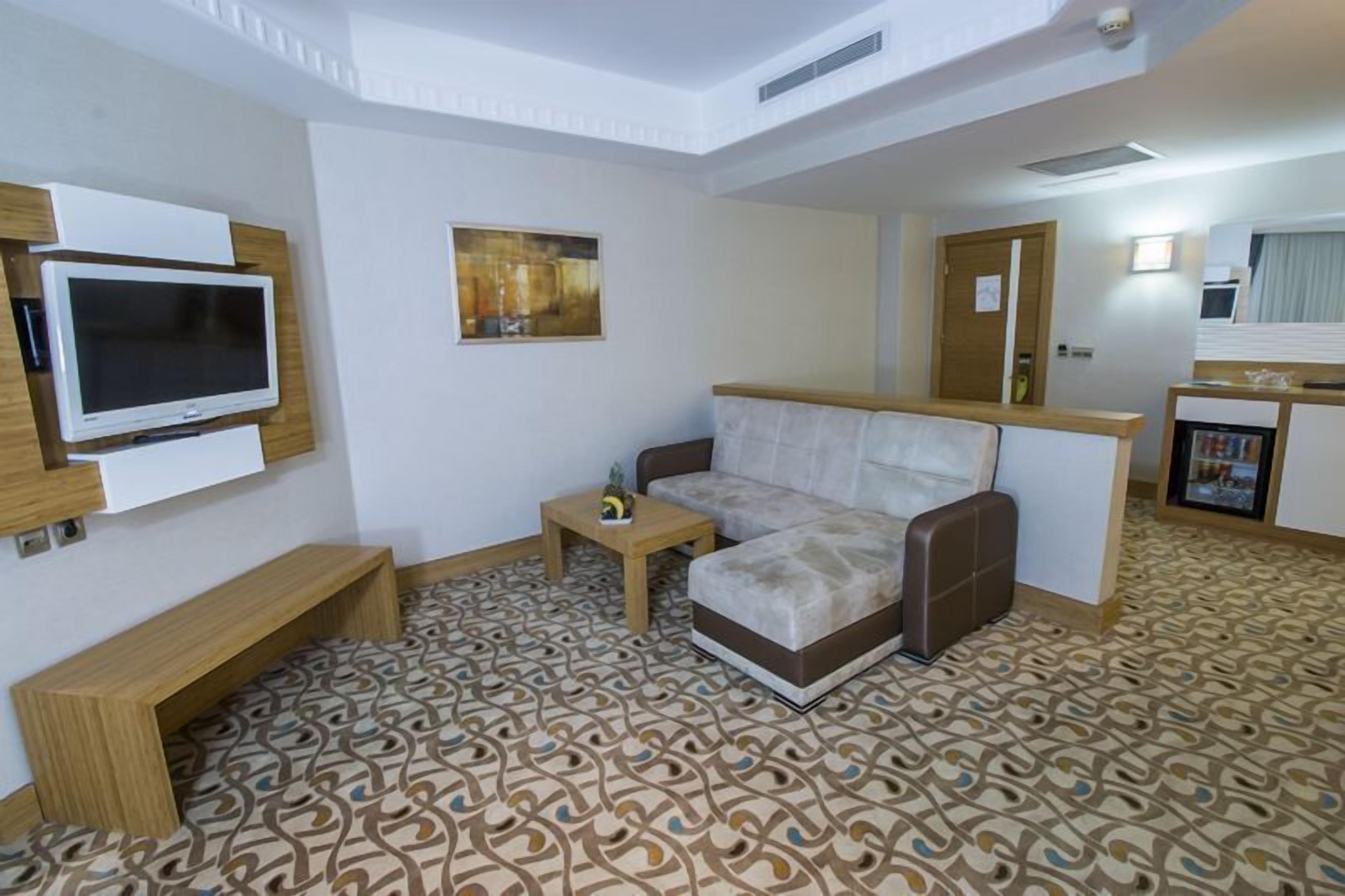 A hotel room with a sofa, a TV mounted on the wall, a small table, and a patterned floor.