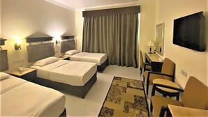 Habitació d'hotel amb dos llits, una taula de treball, una cadira, un televisor i una finestra amb cortines.