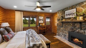 A log cabin room with a bed, a fireplace, a desk, and a view of the outdoors.