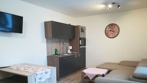 Un espacio habitable compacto con kitchenette, una mesa de comedor, un sofá y un reloj en la pared.