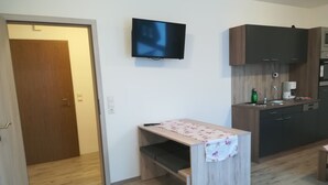 Una cocina compacta con encimera de madera, televisor integrado y armarios oscuros.