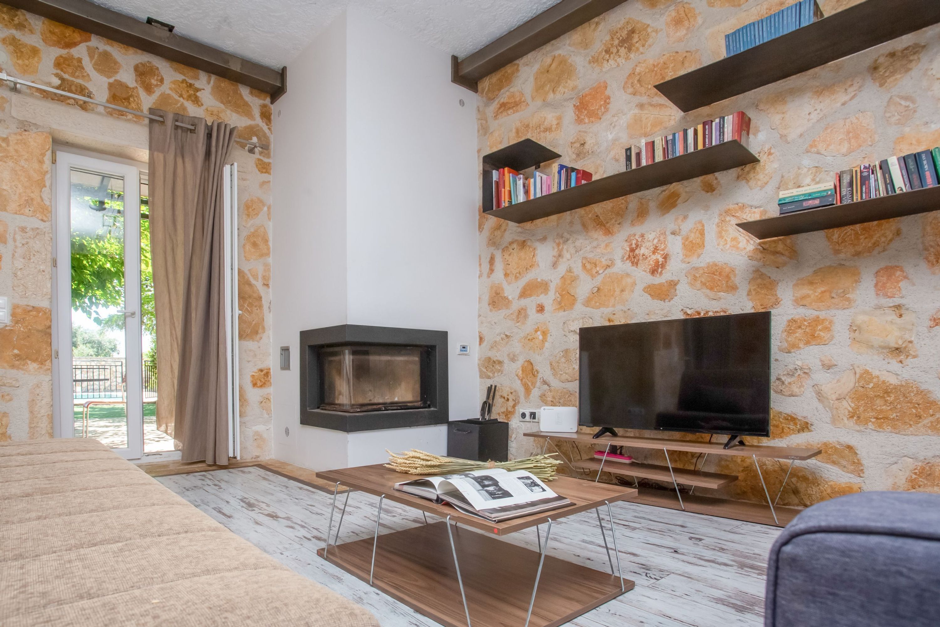 A living room with a stone wall, a fireplace, a TV, and bookshelves.