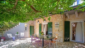 A stone-floored patio with a table and chairs, a potted plant, and a staircase leading to an upper level. - Villa Yiarios in Corfu (Corfu)