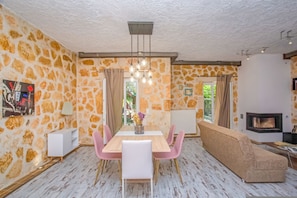 A modern living room with a stone wall, a wooden dining table with pink chairs, a beige sofa, and a fireplace. - Villa Yiarios in Corfu (Corfu)