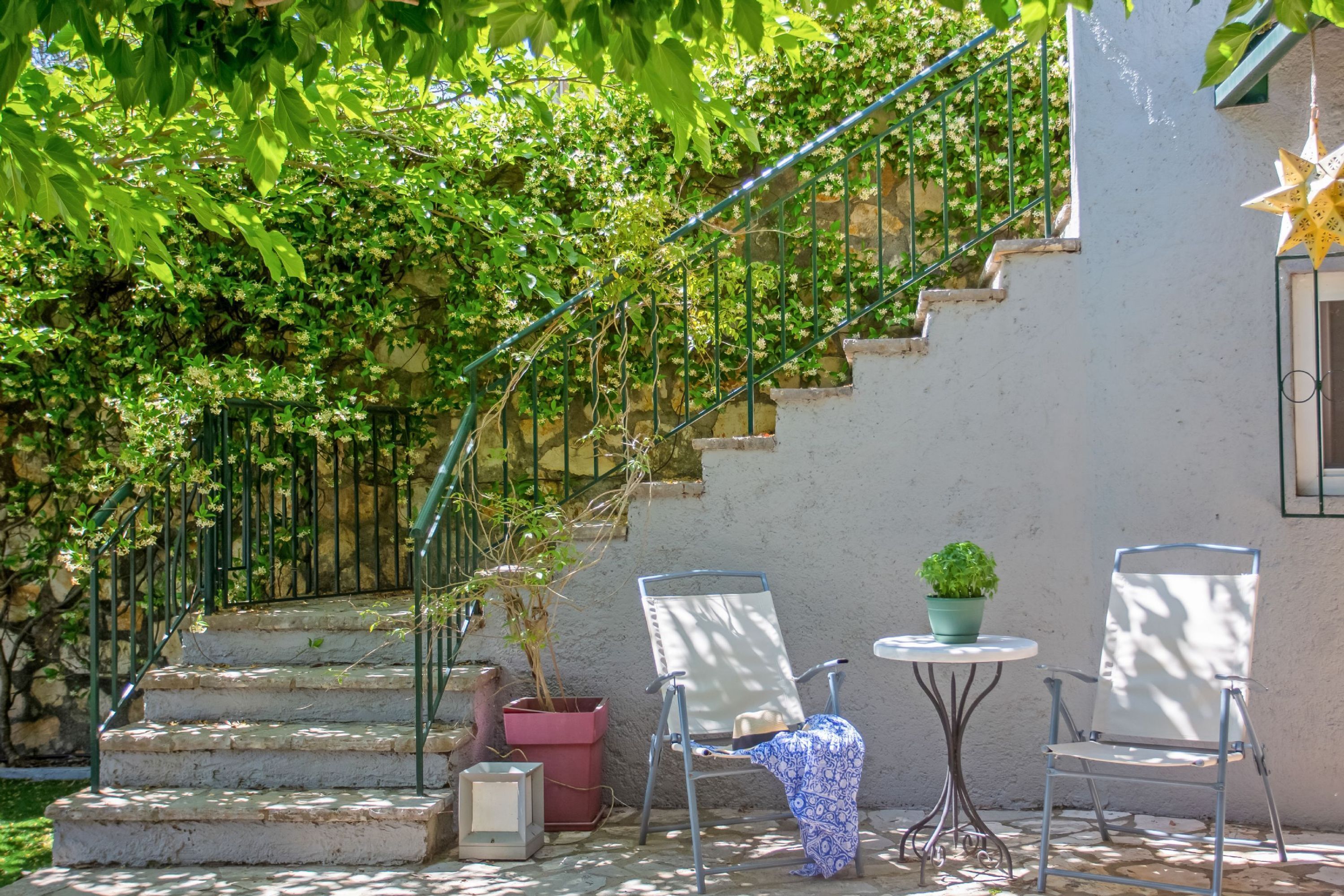 Un espace patio comprenant un escalier, deux chaises, une petite table et une plante en pot.