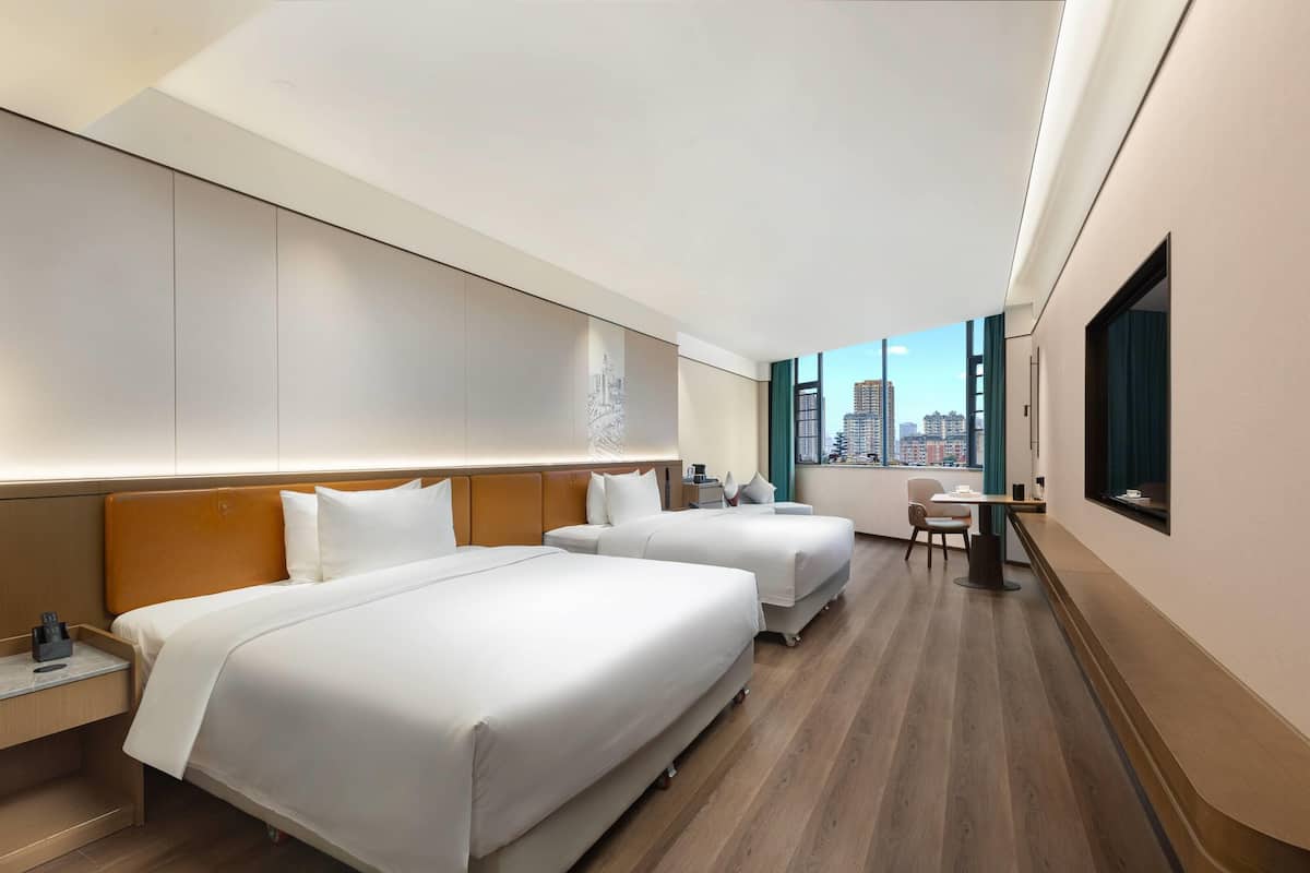 A hotel room with two beds, a desk, and a view of the city.