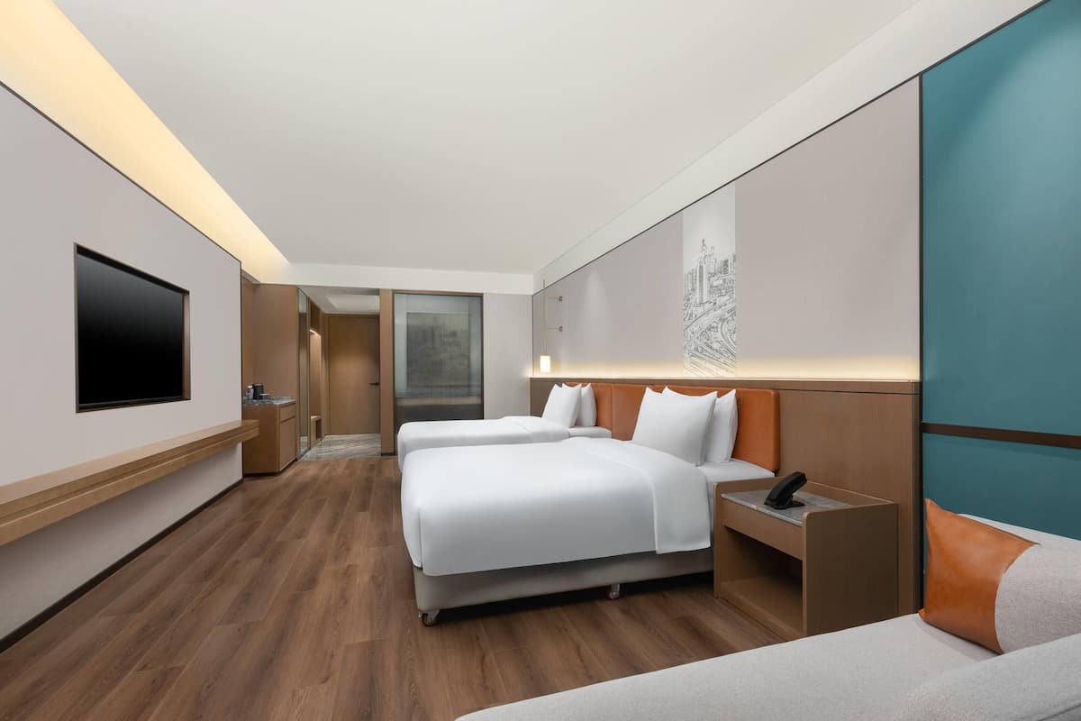 A modern hotel room with two beds, a flat-screen TV, a desk, and a large window.