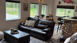 Een ruime woonkamer met een grote zwarte leren bank, een kamerkleed met een patroon en een wand van natuursteen.