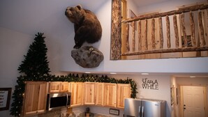 Een keuken met houten kastjes, een opgehangen berenbeeld, een rustieke houten balk en een kerstboom.
