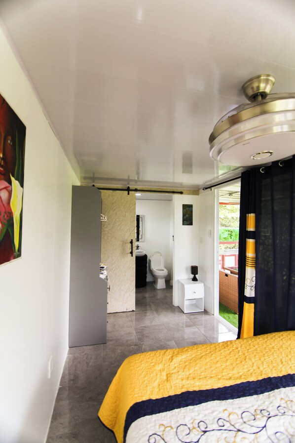 Habitación de hotel con cama, baño con inodoro y lavamanos, y pasillo que conduce a otra habitación.