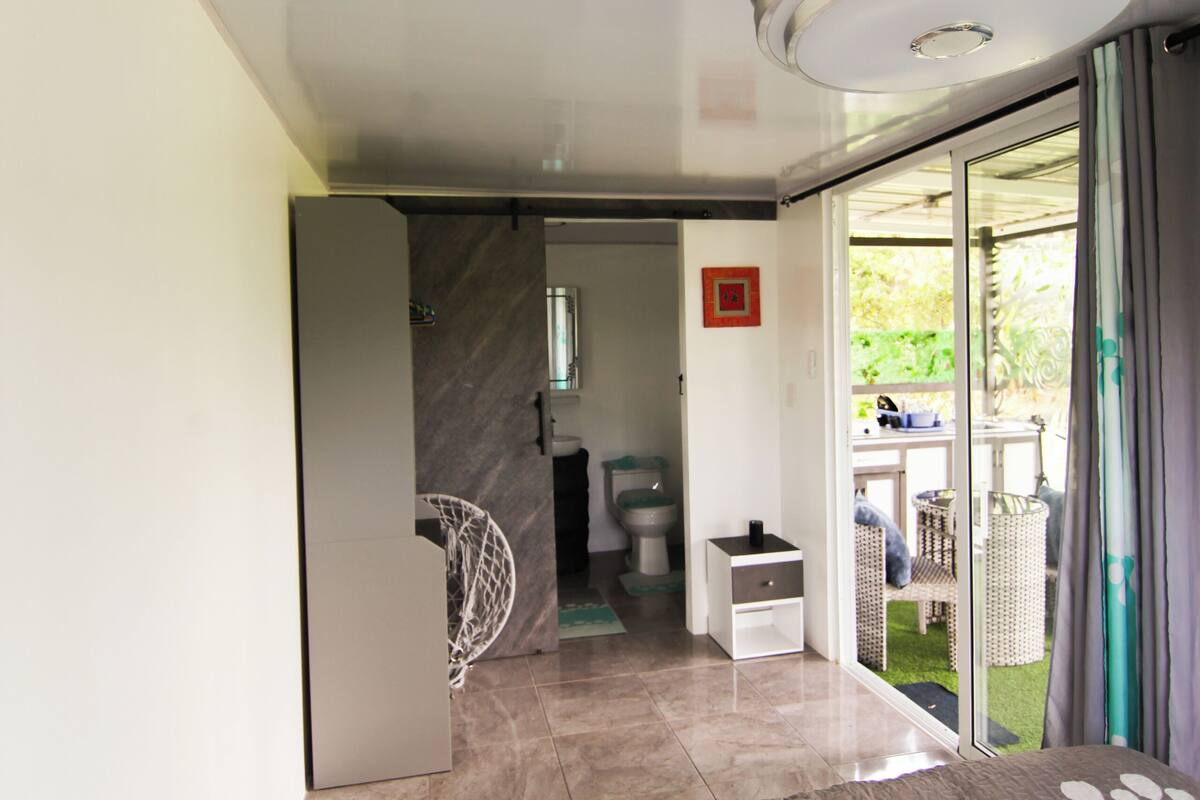 A bedroom with a bed, a ceiling fan, a sliding glass door leading to a balcony, and a bathroom visible through an open door.