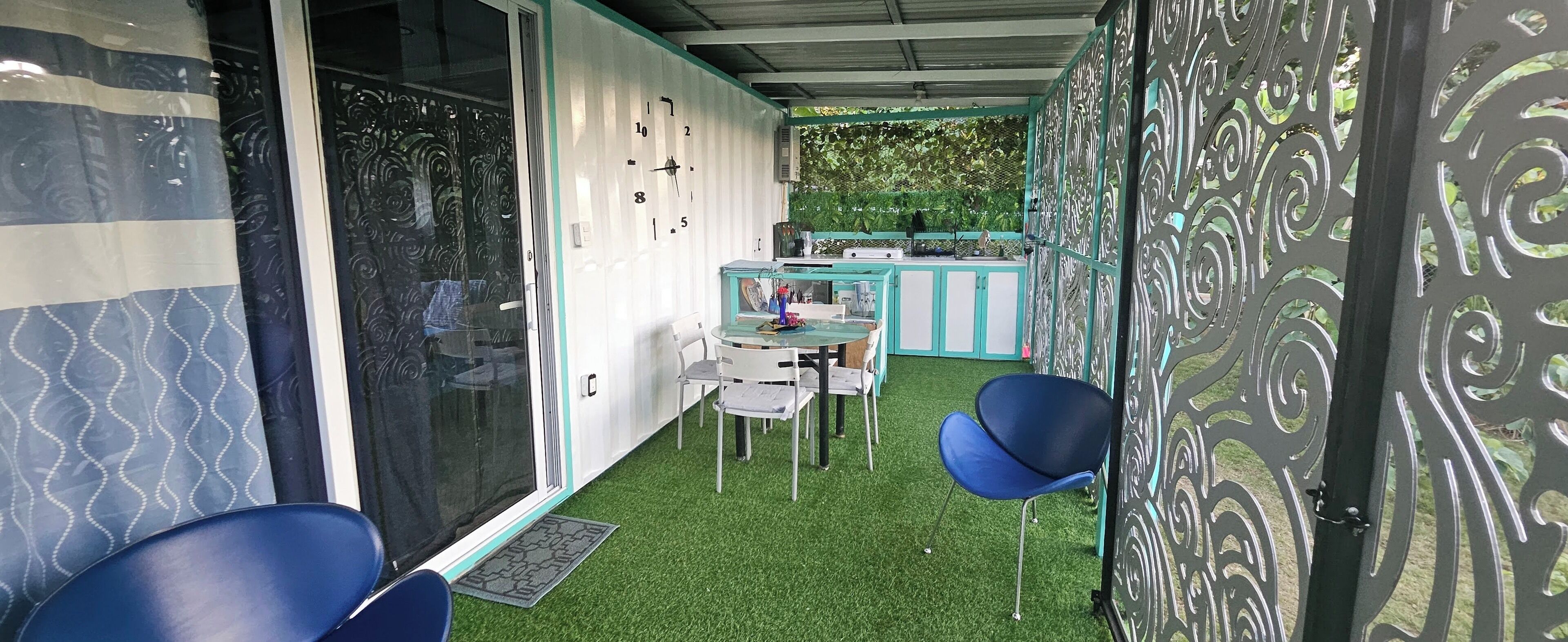 A room with a glass door, a small table with chairs, and a decorative wall with a clock.