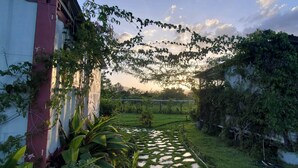 Un giardino con un vialetto, vegetazione e un edificio con una parete rossa.