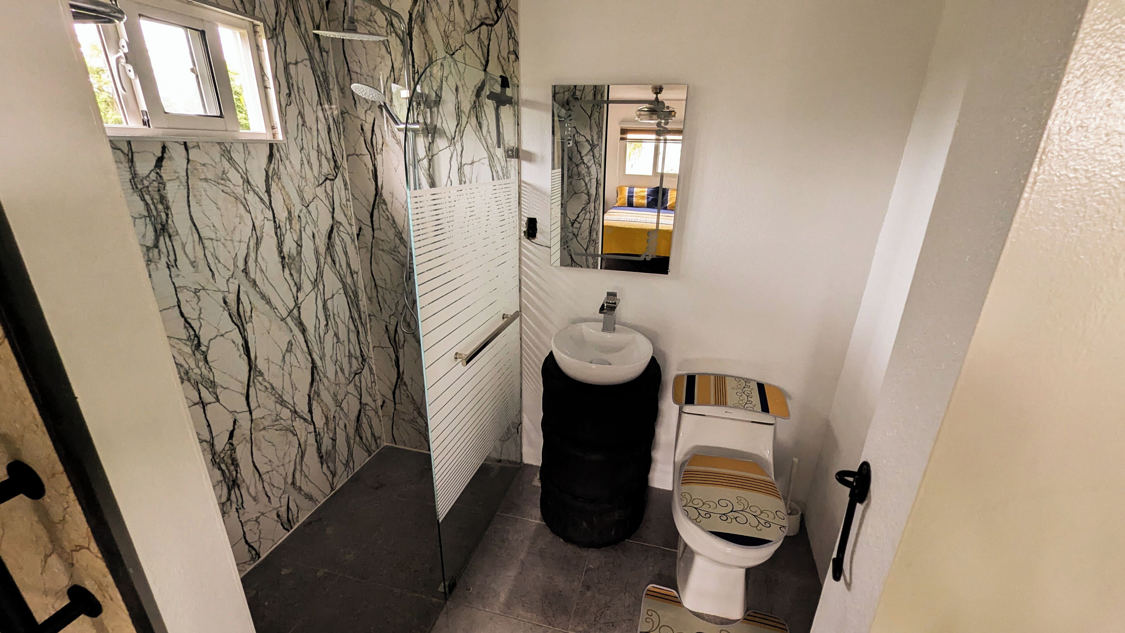 Un baño con pared de mármol, ducha, inodoro y espejo.