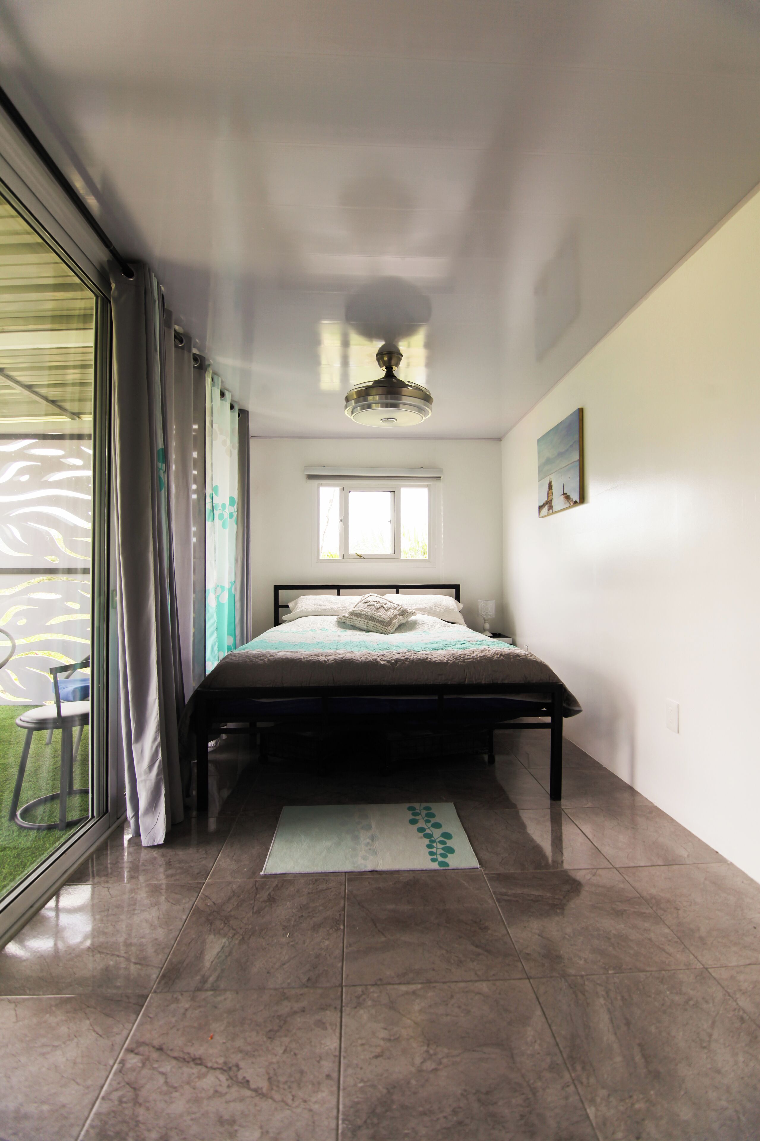 Une chambre à coucher avec un lit, une fenêtre, un ventilateur de plafond et une vue sur un balcon.