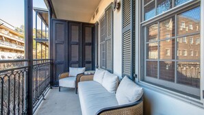 Un balcón con sofá y sillones, baranda y vista a edificios.