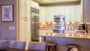 Una cocina moderna con armarios blancos, electrodomésticos de acero inoxidable y una isla central con taburetes.