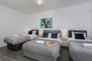 A modern hotel room with three beds, a large abstract painting, and a breakfast tray on the central bed.