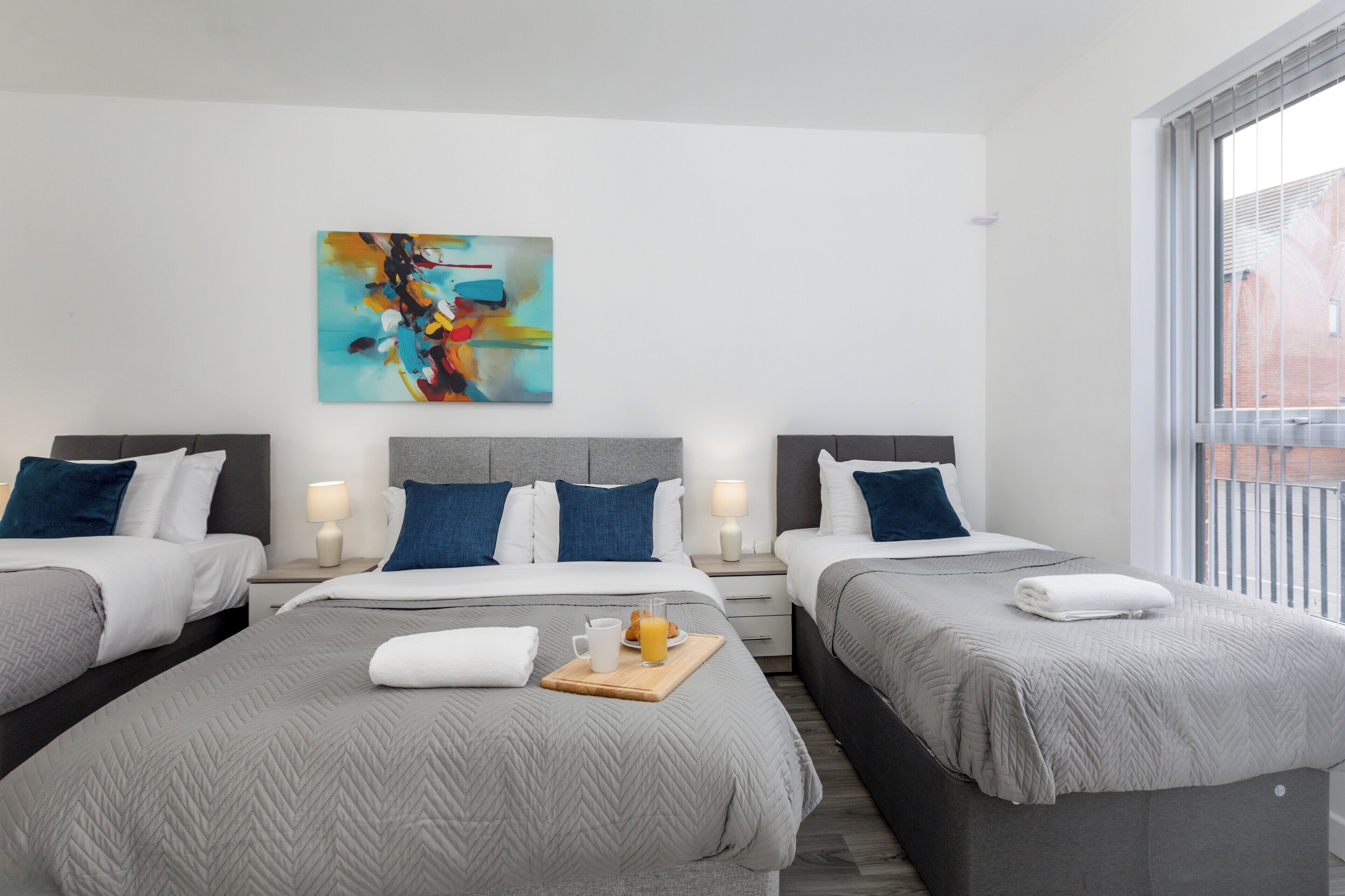 A hotel room with two beds, a modern abstract painting, and a breakfast tray with orange juice.