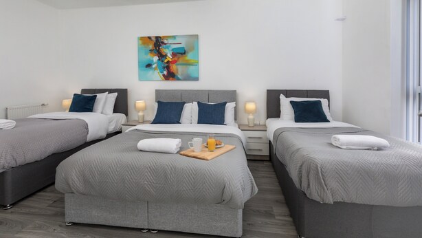 Ein Hotelzimmer mit drei Betten, einem modernen abstrakten Gemälde und einem Frühstücksbrettchen auf dem größten Bett.