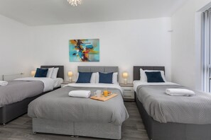 A hotel room with three beds, a modern abstract painting, and a breakfast tray on the largest bed. - House - Sleeps 10 - Parking - Wifi (Sheffield)