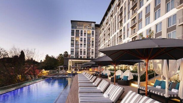 Ein Poolbereich mit Liegestühlen und Sonnenschirmen, ein klarer Himmel und ein Hotelgebäude im Hintergrund.