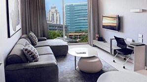 Ein modernes Hotelzimmer mit großem Fenster, einer Couch, einem Couchtisch, einem Fernseher und einem Schreibtisch mit Stuhl.