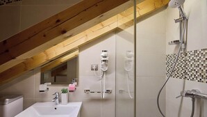 Ein Badezimmer mit einem weißen Waschbecken, einem Spiegel, einer Dusche inklusive Duschbrausehandstück und einer gefliesten Wand mit Mosaikmuster.
