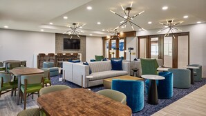 A hotel lobby with a seating area, tables, and a TV screen. - SpringHill Suites by Marriott St. Louis Chesterfield (Chesterfield)