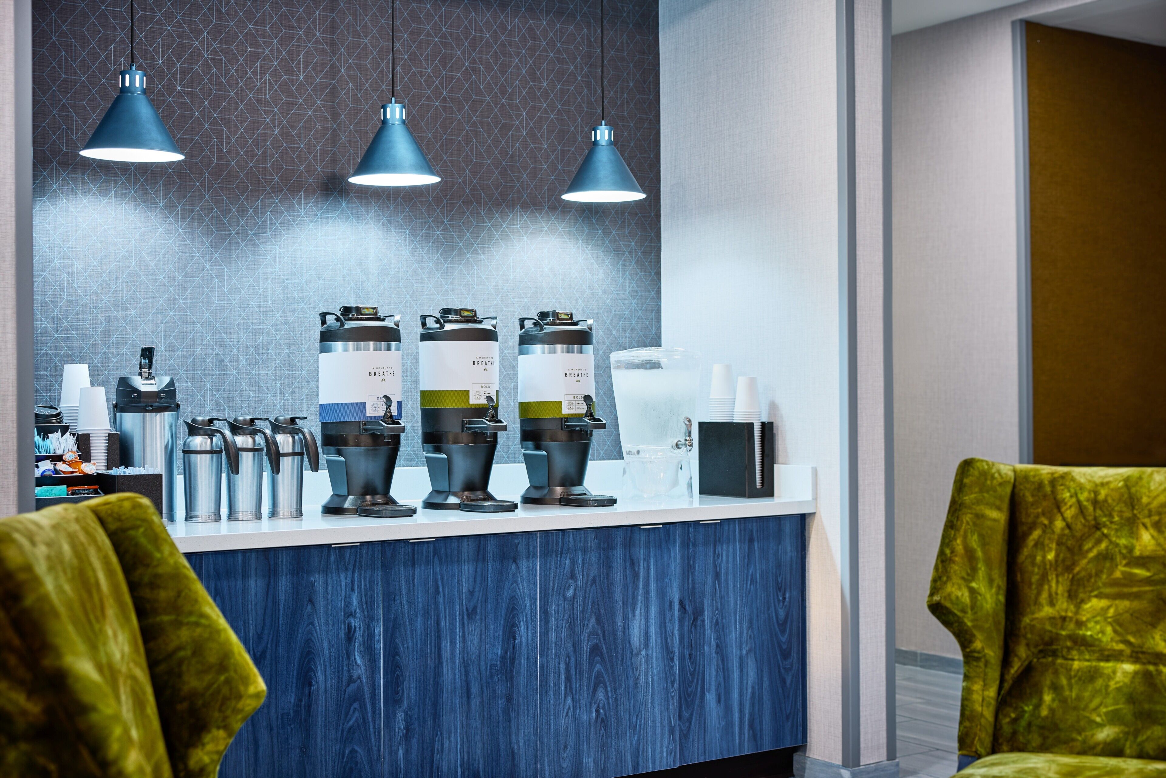 Un espace d’accueil avec un comptoir, des bouilloires et une machine à café. Trois lampes suspendues sont fixées au-dessus du comptoir.