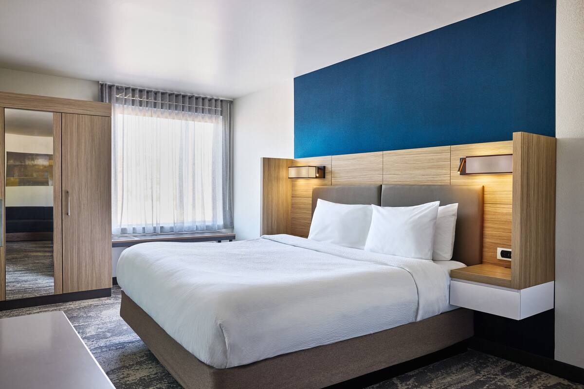 A hotel room with a bed, bedside tables, a wardrobe, and a window with curtains.