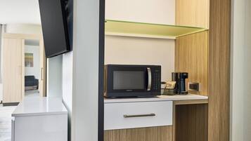 A modern kitchen with a microwave, coffee maker, and a glass shelf.