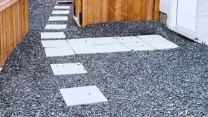 A pathway leading to a wooden gate, surrounded by gravel and a white wall.