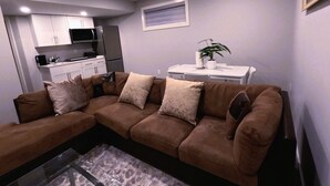 A living room with a brown sectional sofa, a small white table, and a potted plant.