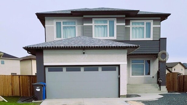 A two-story house with a grey garage door, a covered driveway, and a wooden fence in the background.