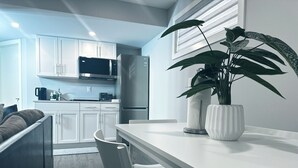 A modern kitchen with white cabinets, a stainless steel refrigerator, a microwave, and a dining area with a white table and chairs.