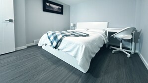 A modern bedroom with a bed, bedside table, lamp, and a desk with a chair.