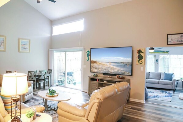 A living room with a sofa, a coffee table, and a television. There is a window with a view of the outdoors.
