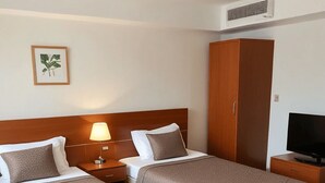 A hotel room with two beds, a wardrobe, a TV, and a framed plant on the wall. - PH Recoletos (Caracas)