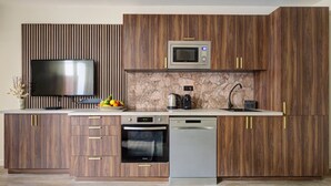 A modern kitchen with a built-in microwave, oven, and dishwasher, wooden cabinets, and a flat-screen TV.