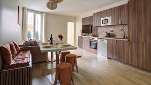 A modern kitchen with wooden cabinets, a dining area with a sofa and stools, and a large window providing natural light.