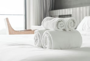 A neatly made bed with rolled white towels and a wooden chair in the background. - B&B THE SEA - Family Rooms (Tropea)