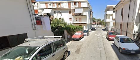 A narrow street lined with parked cars and multi-story residential buildings.