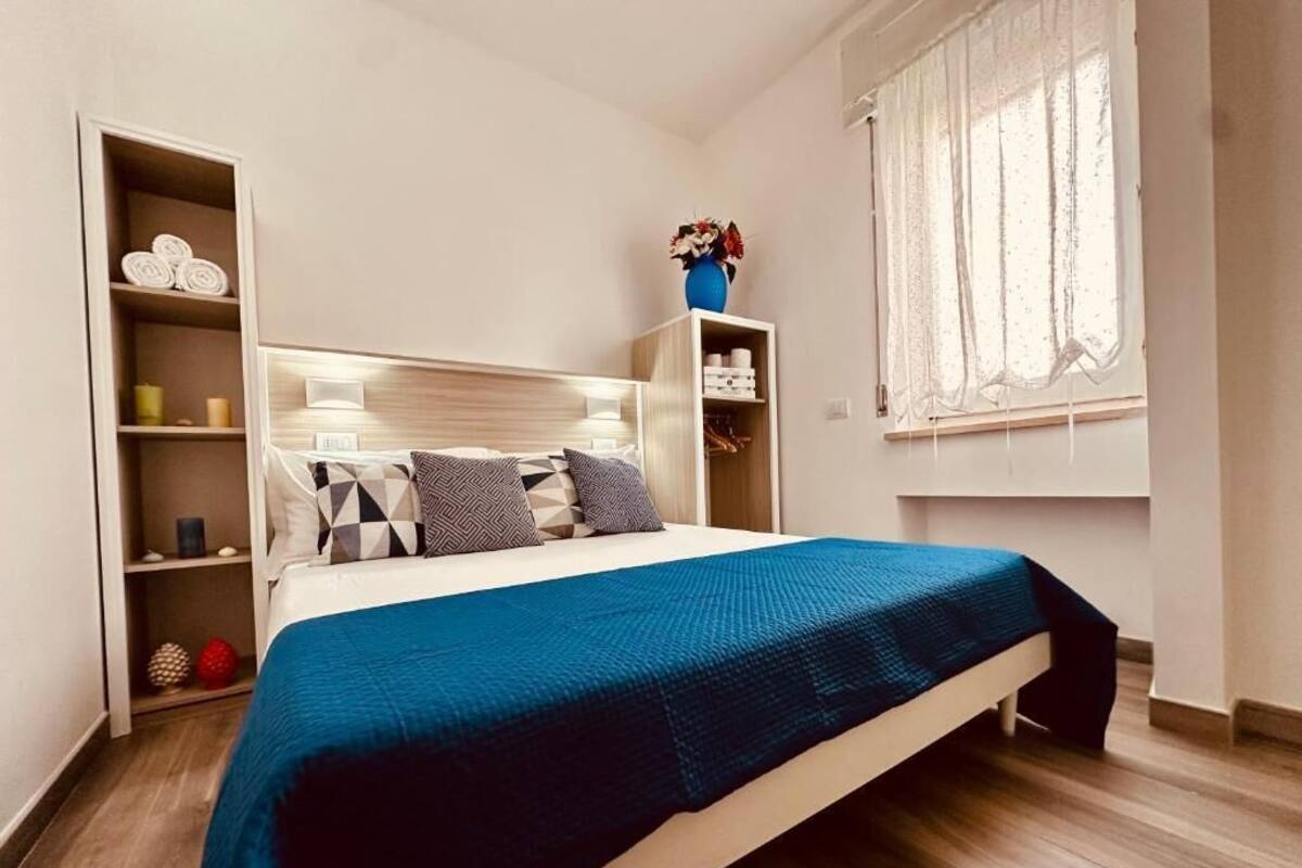Een slaapkamer met een bed, een kledingkast, een plank met handdoeken en een raam met gordijnen.