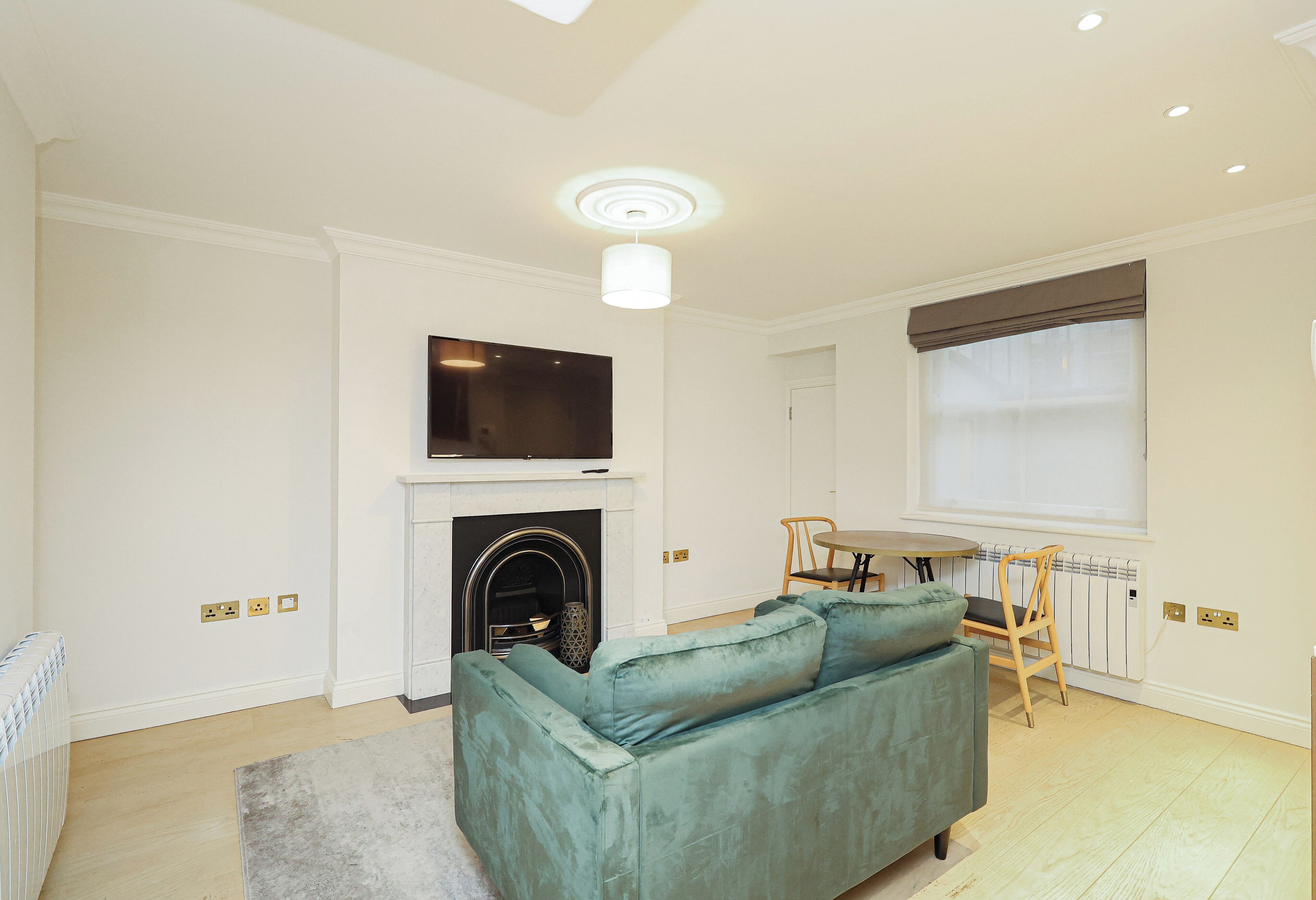Una sala de estar con un sofá verde, una chimenea, un televisor montado encima y una zona de comedor con mesa y sillas.