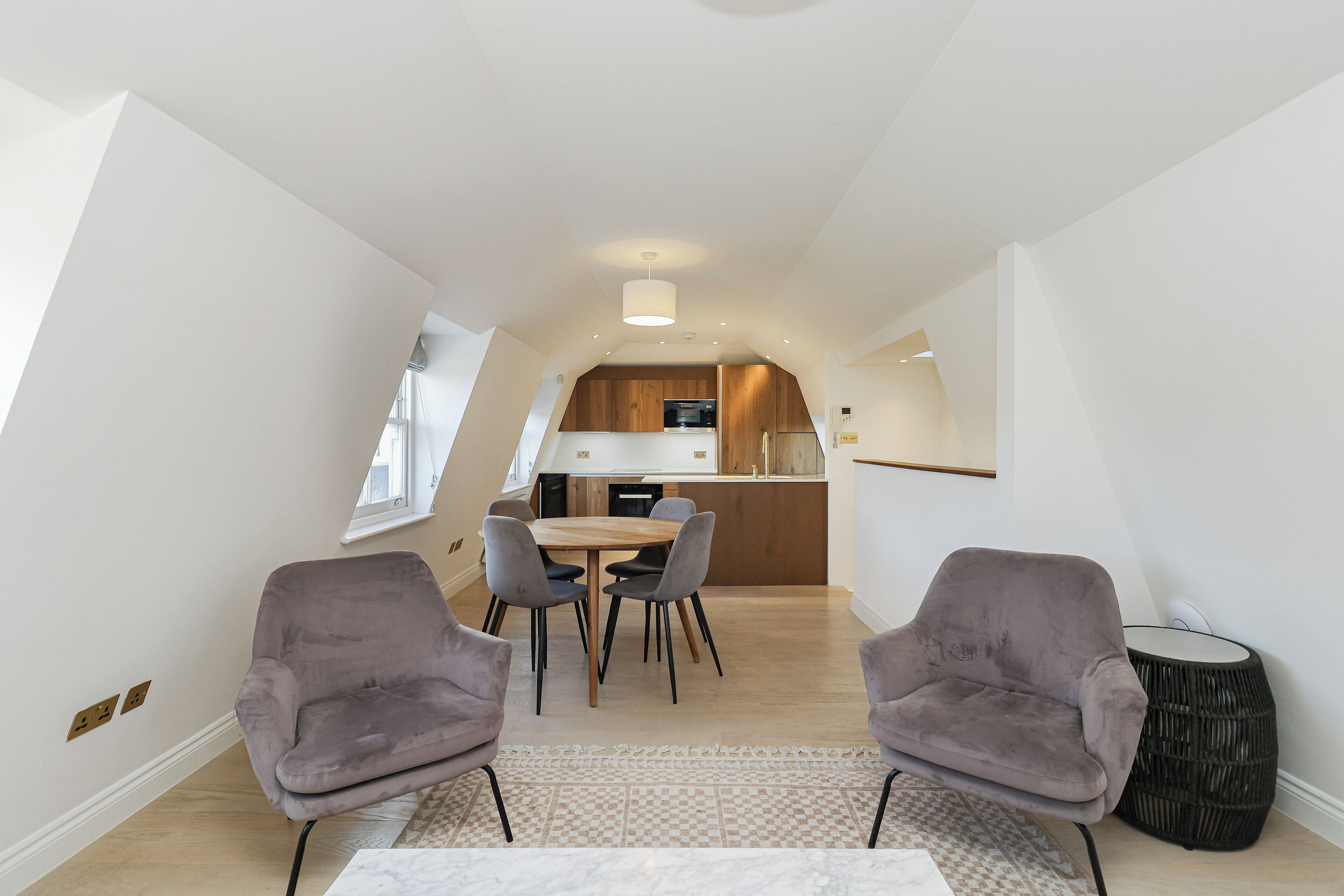 Eine moderne Küche mit Holzausstattung und einer zentralen Kochinsel, ein Essbereich mit Tisch und Stühlen sowie eine gemütliche Sitzecke mit zwei Sesseln.